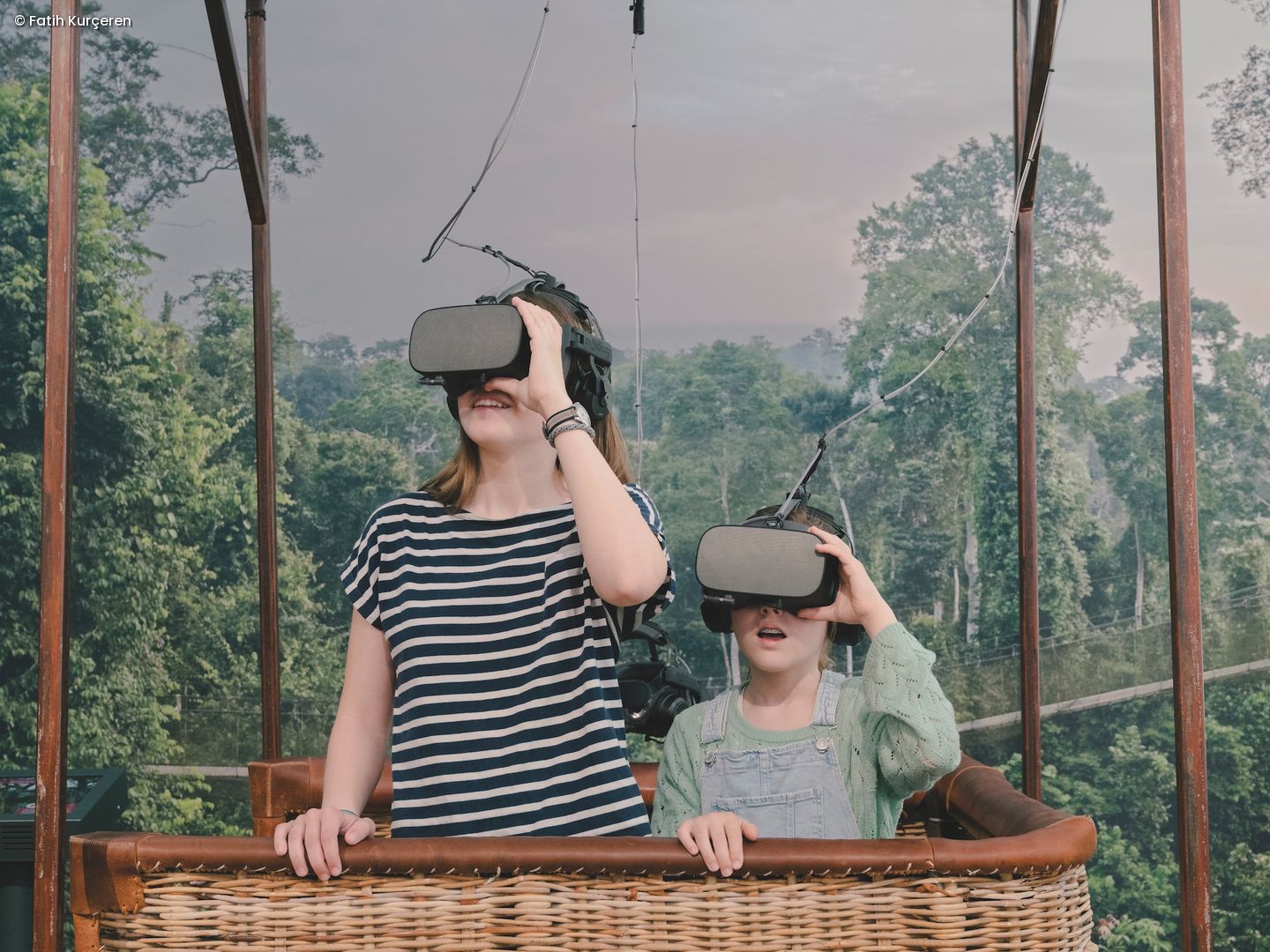 Zwei Kinder im Korb eines Ballons fliegen über den Dschungel und tragen VR-Brillen