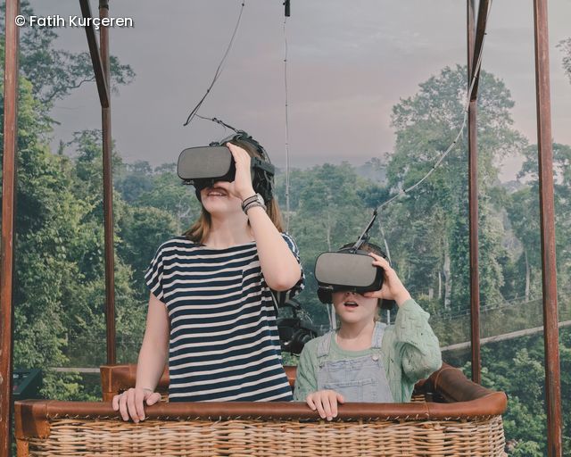 Zwei Kinder im Korb eines Ballons fliegen über den Dschungel und tragen VR-Brillen