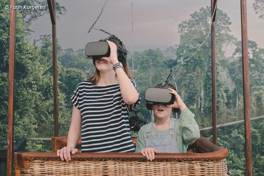 Zwei Kinder im Korb eines Ballons fliegen über den Dschungel und tragen VR-Brillen